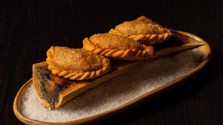 Three golden fried pastries served on a split piece of bamboo